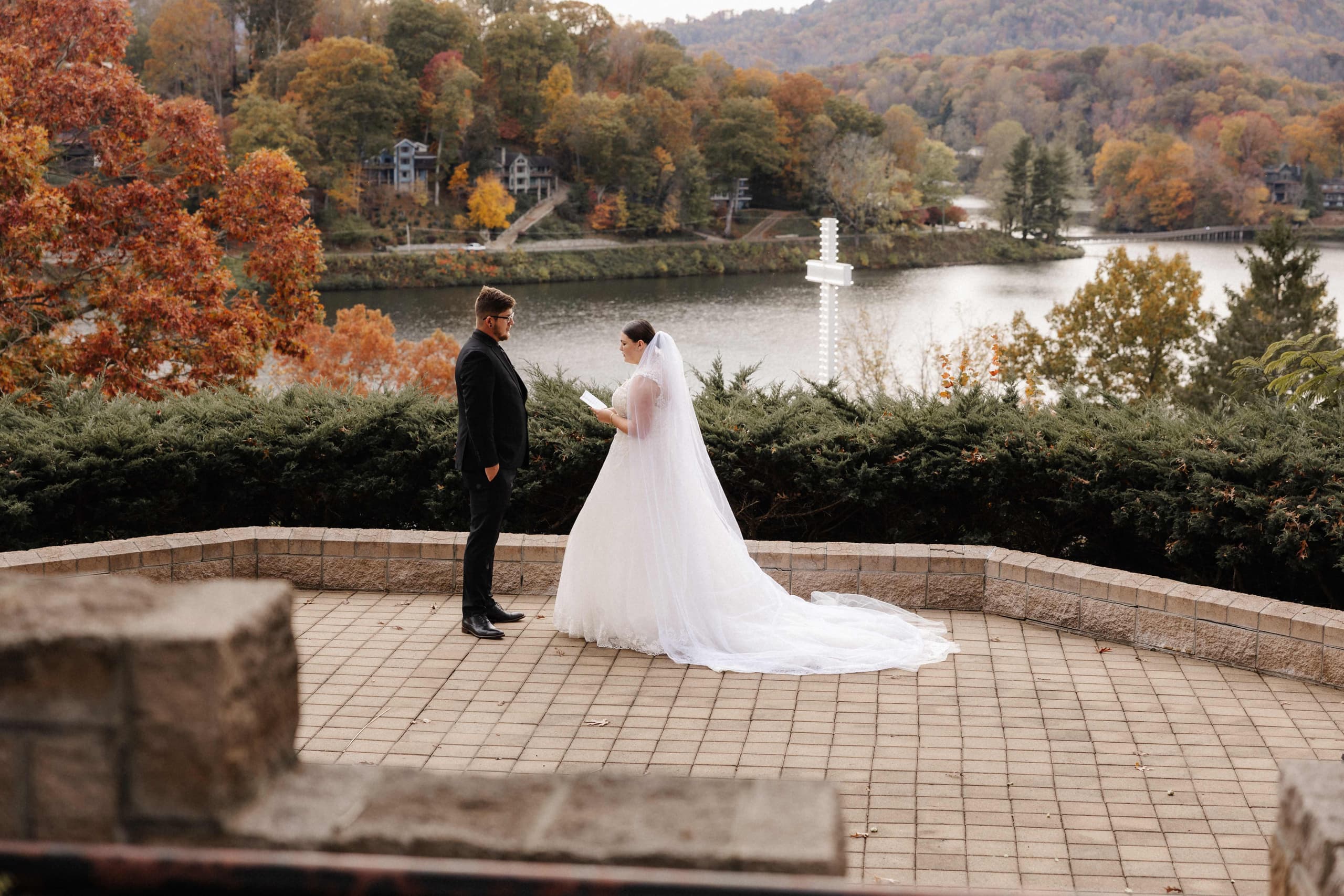 Bride reading vows to groom on a stone terrace overlooking a lake framed by autumn mountains