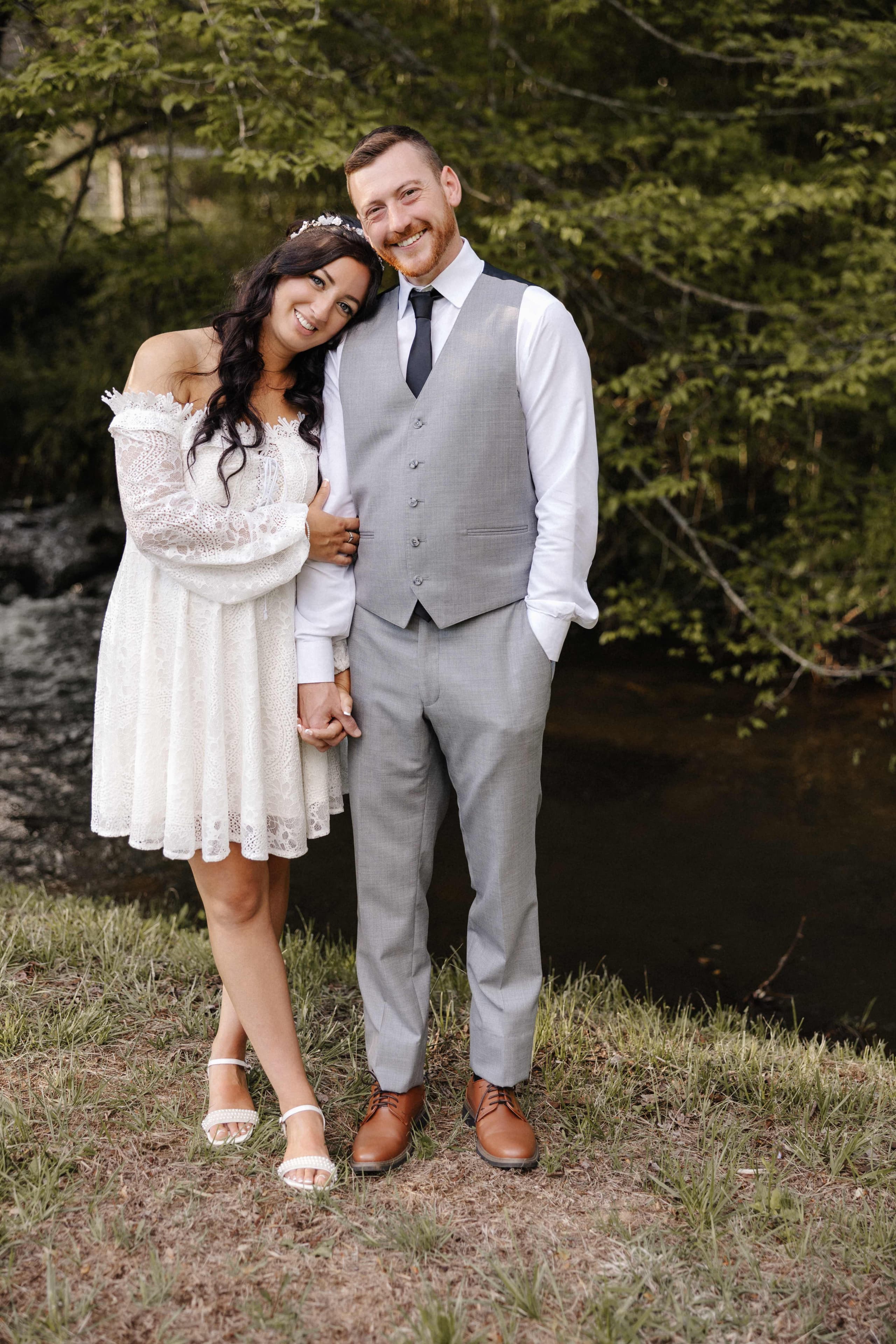 Couple portrait by river with bride in short lace dress