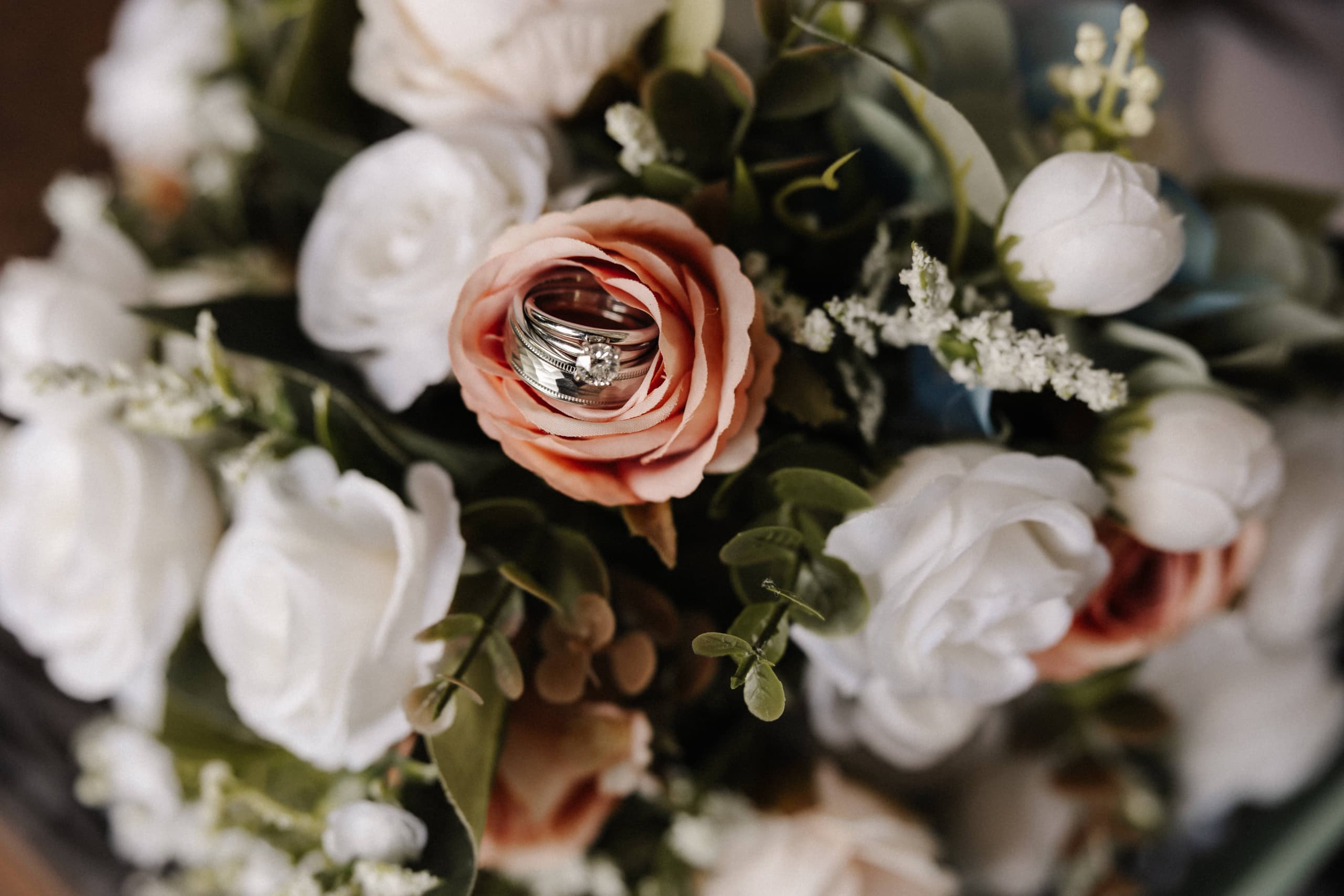 Wedding rings in pink rose with white roses and greenery