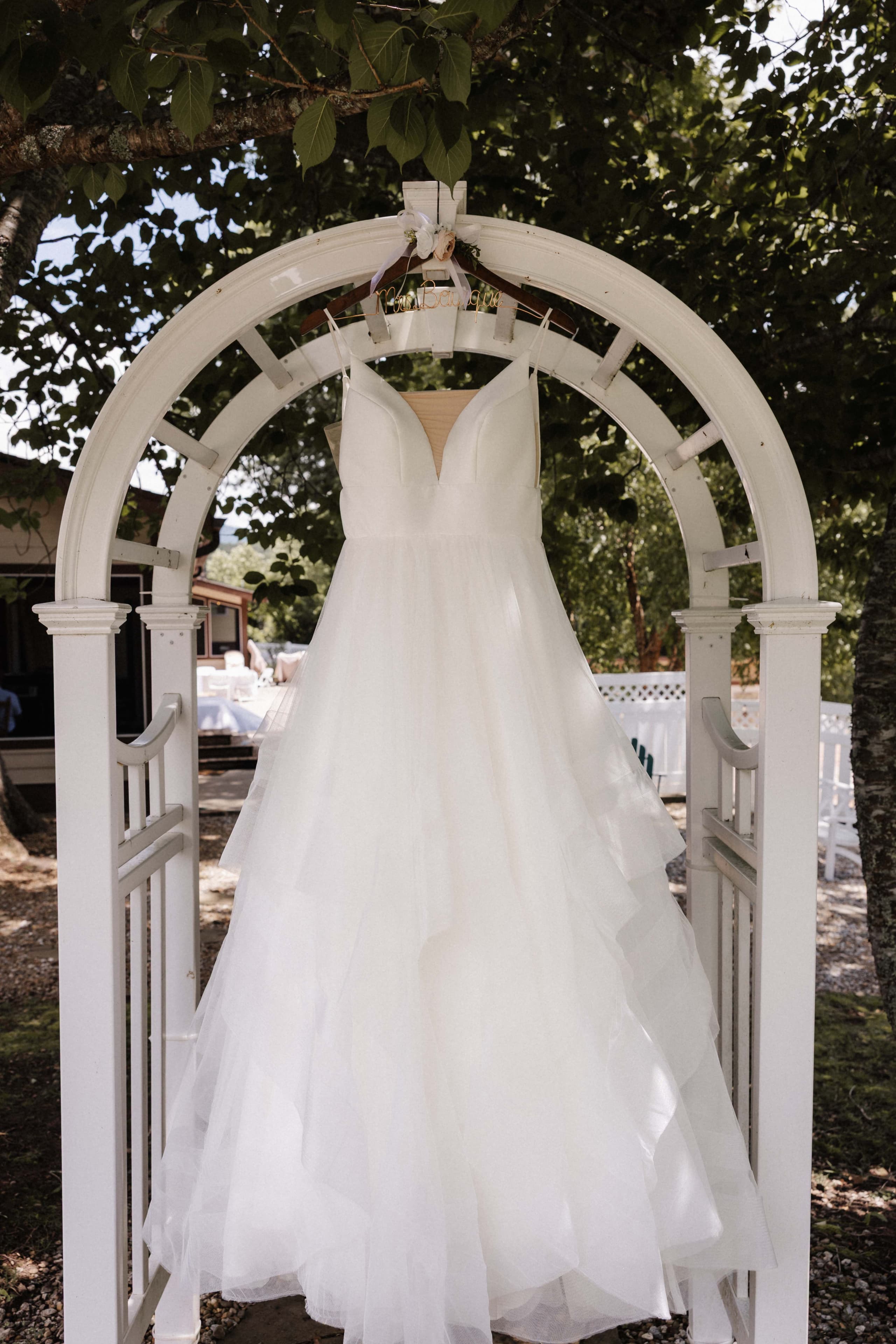 Tulle ballgown hanging on white arbor under tree canopy