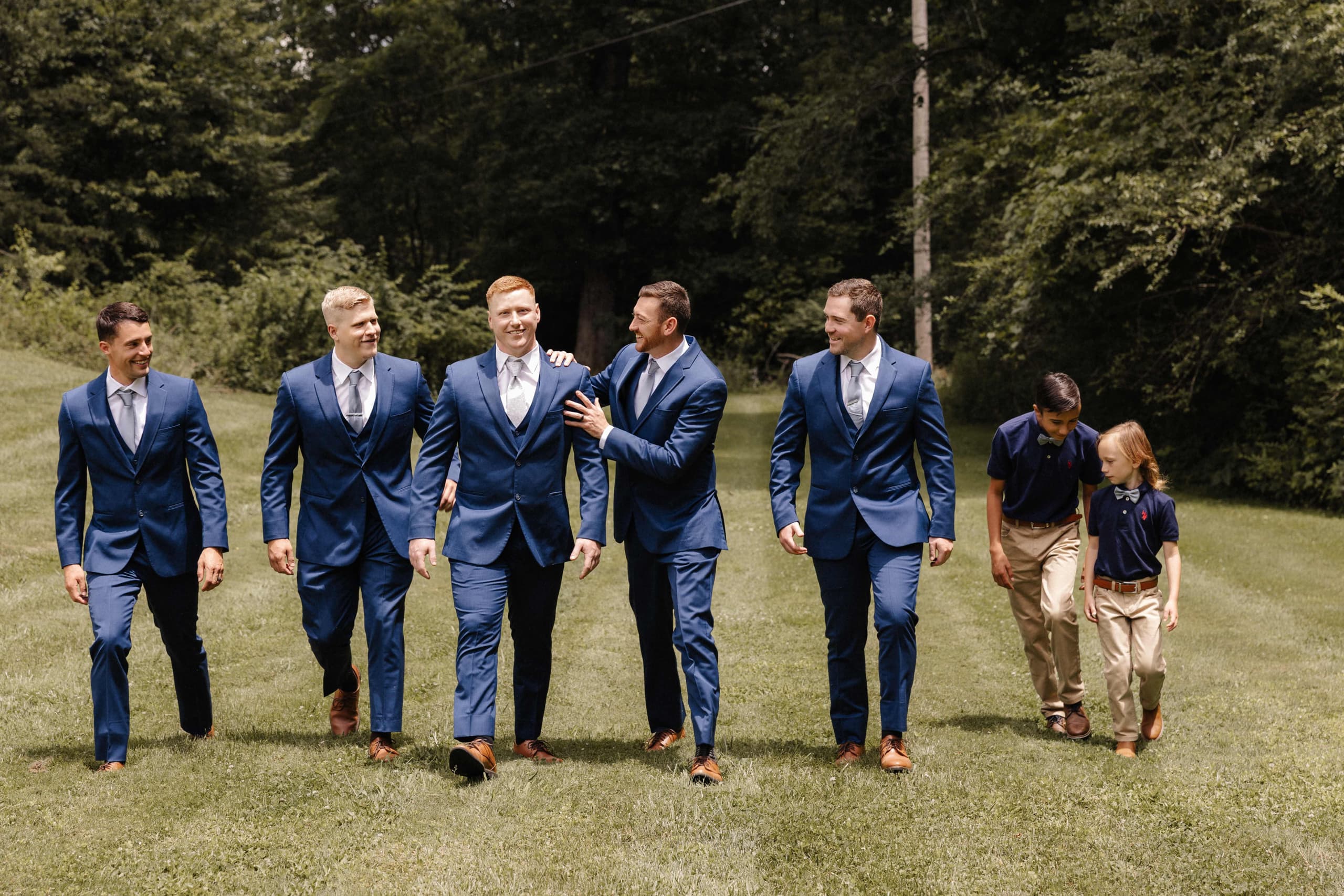 Groomsmen walking in navy suits with young ring bearers