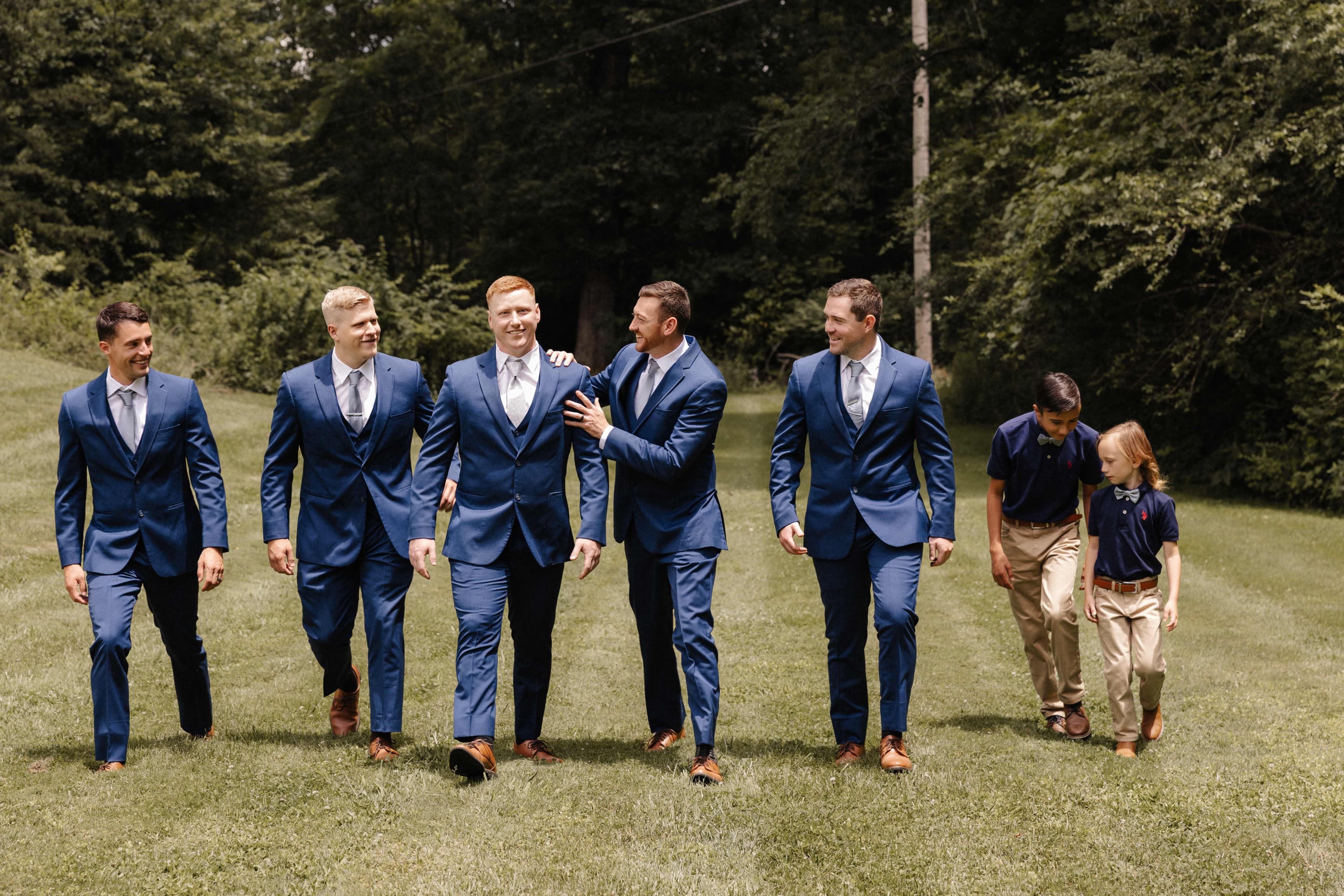 Groomsmen walking in navy suits with young ring bearers