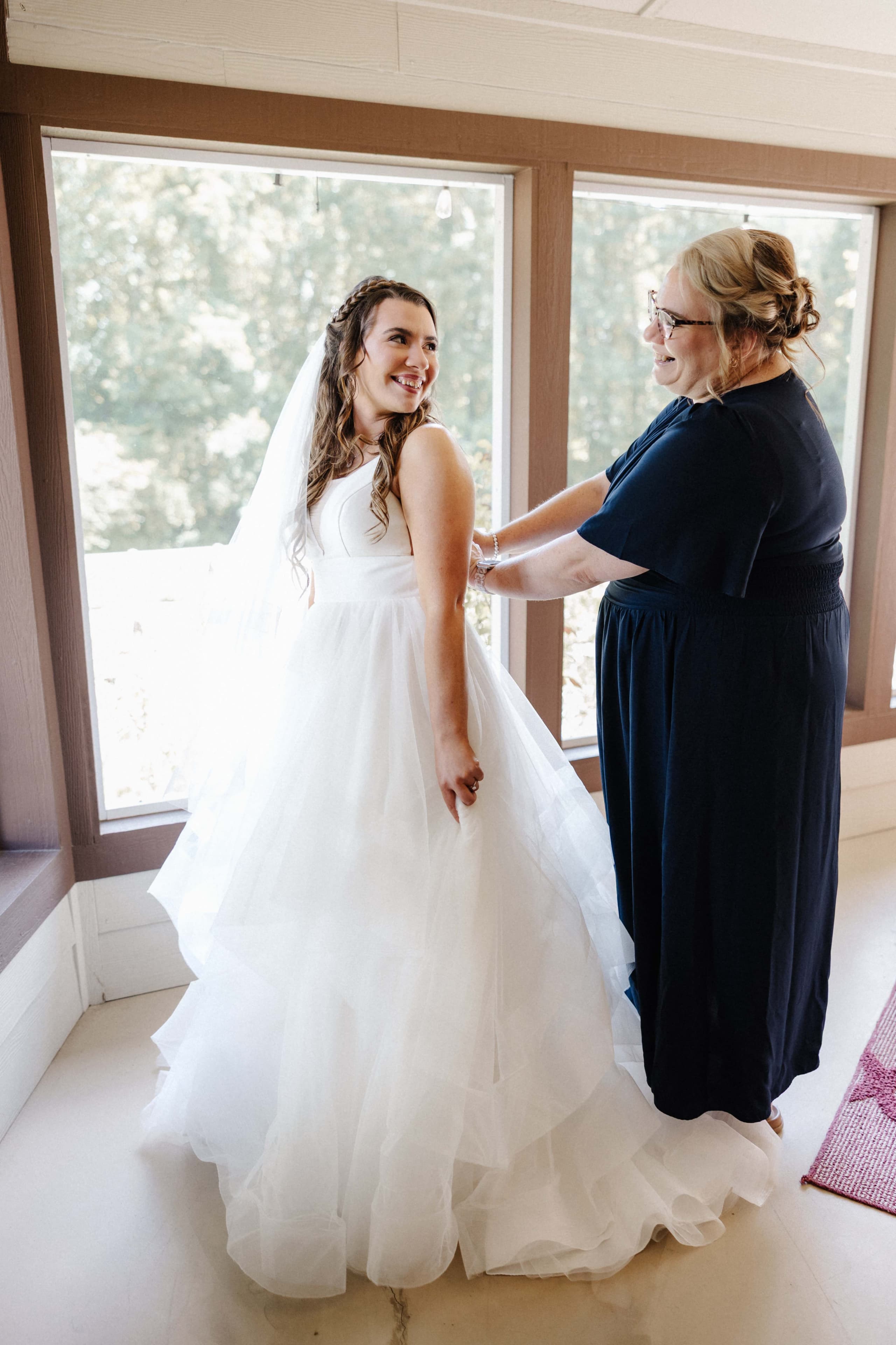 Mother helping bride with dress in window light