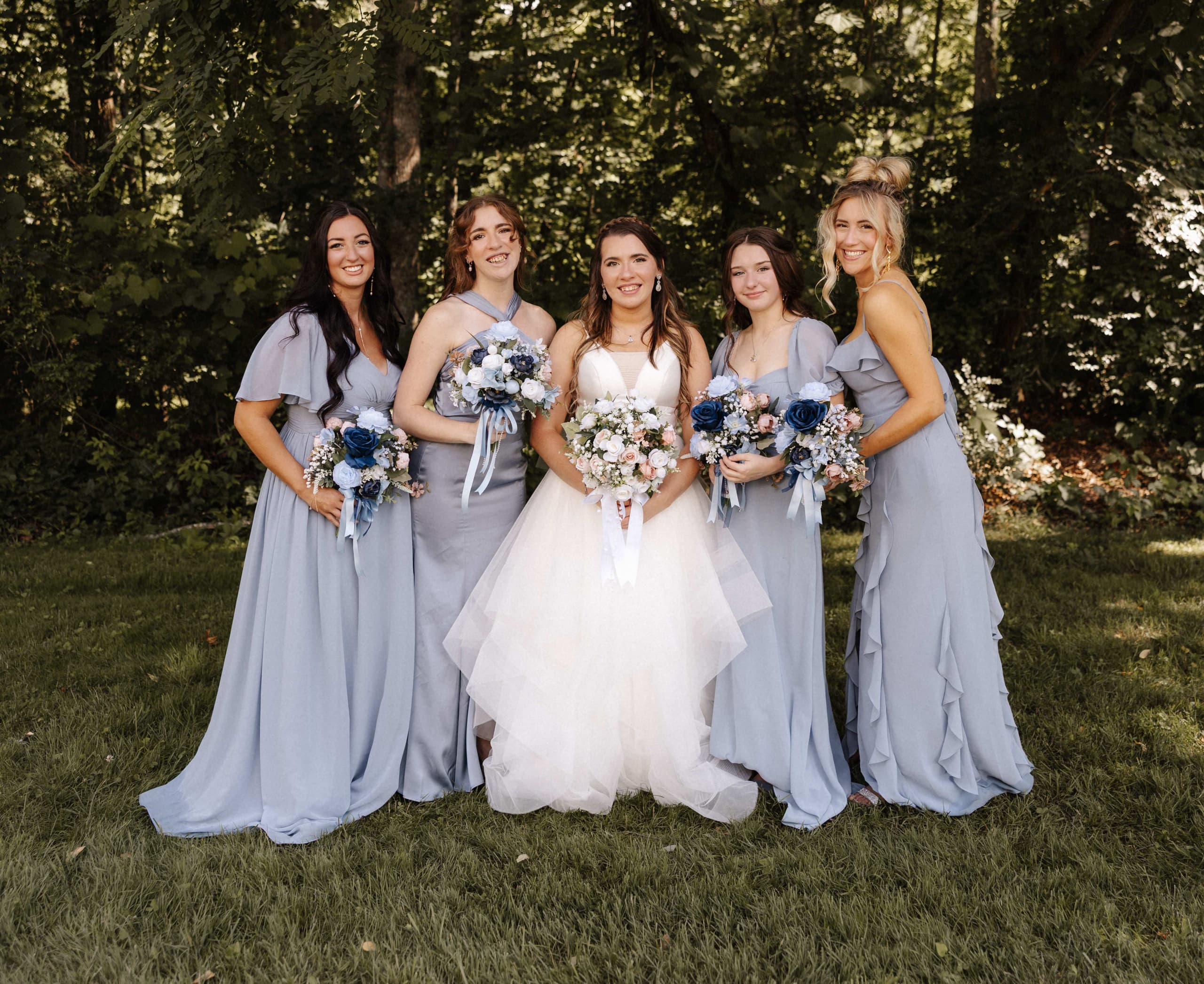 Bride with bridesmaids in dusty blue dresses holding bouquets