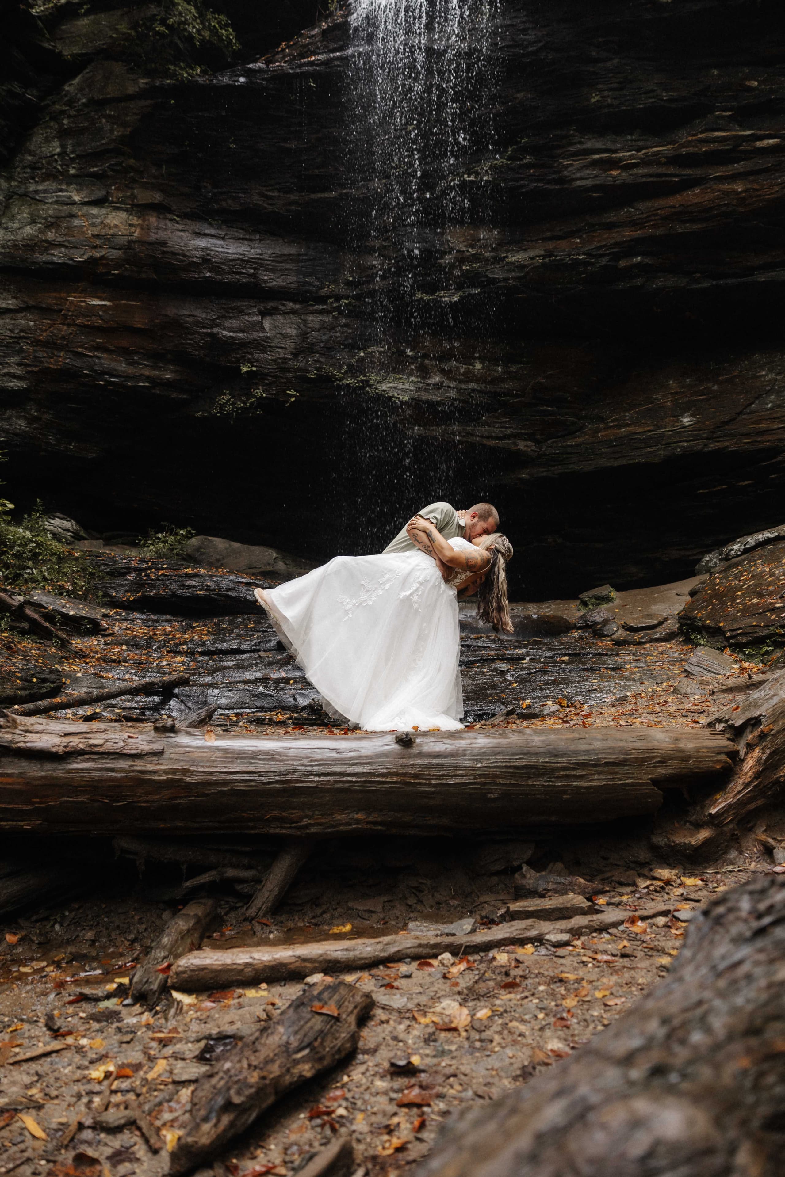 Dramatic dip kiss at waterfall base on fallen log
