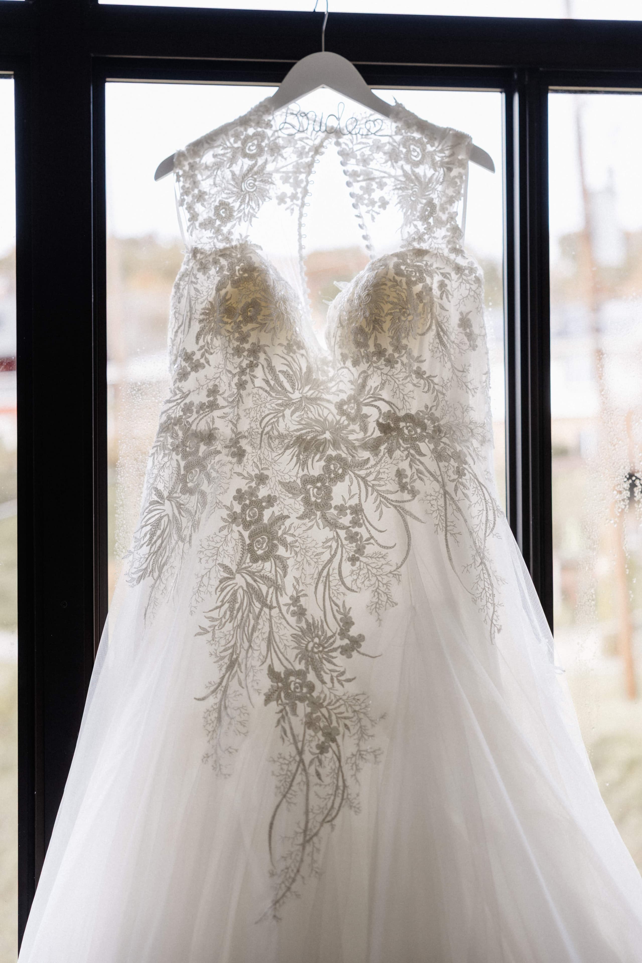 Lace wedding dress detail hanging in window with Bride hanger