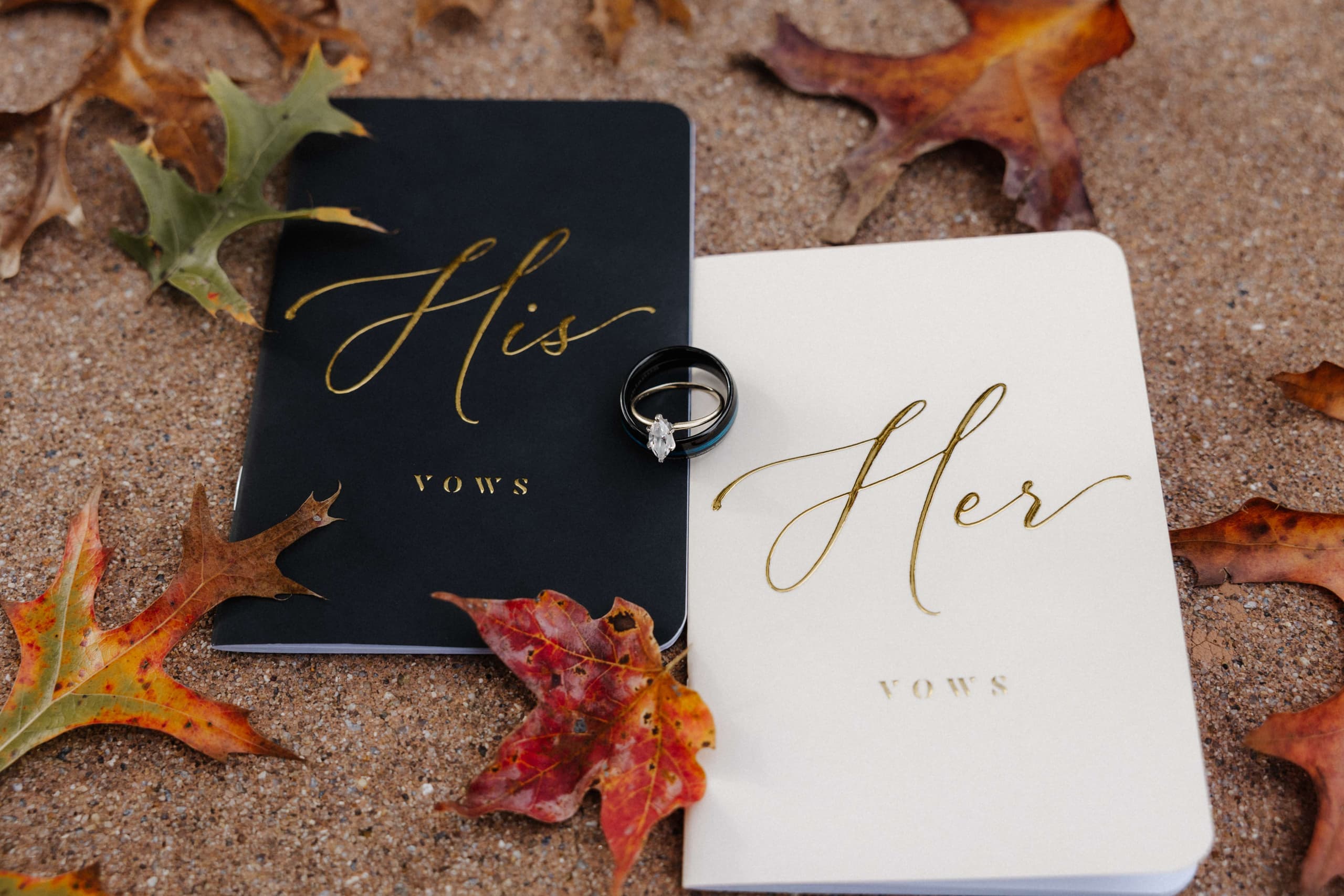 His and Her vow books with rings on sand with fall leaves