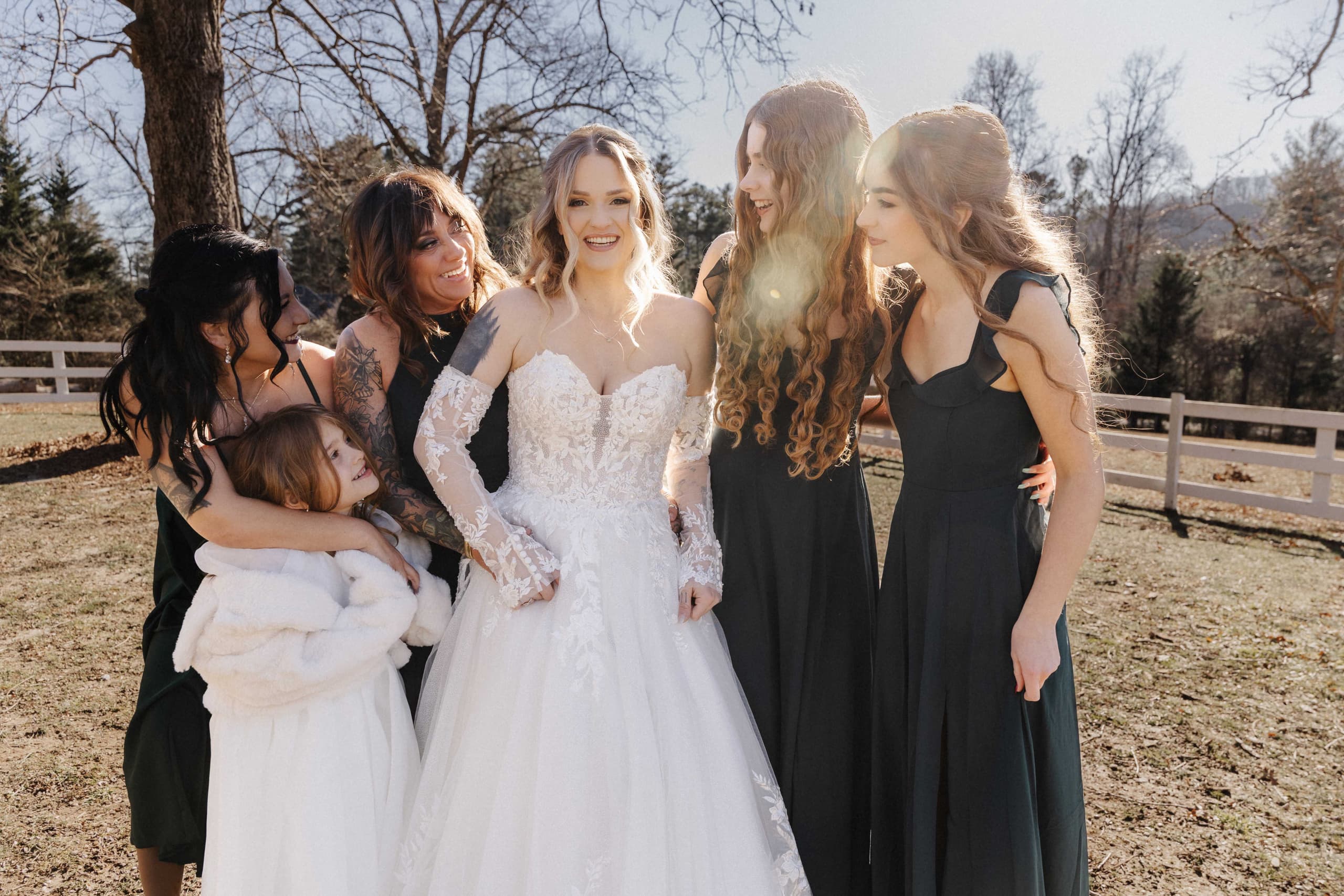 Bride laughing with bridesmaids in black dresses with golden hour backlight