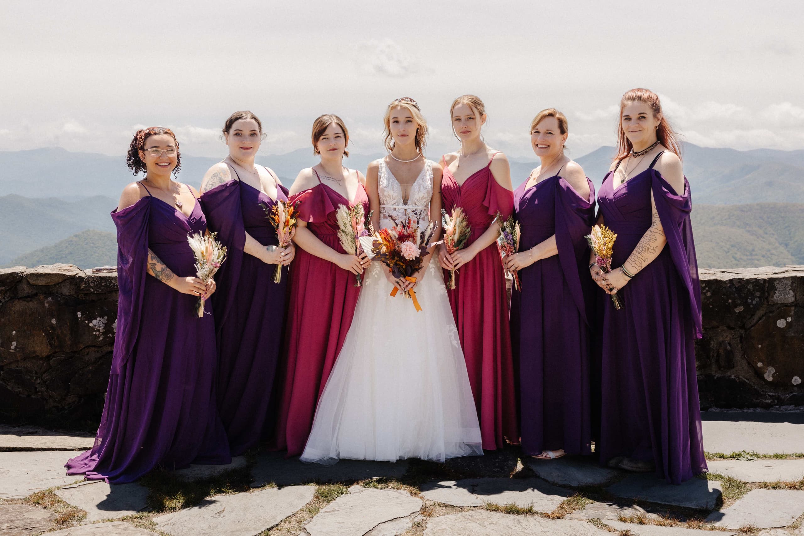 Bride with bridesmaids in purple and magenta dresses with dried flower bouquets