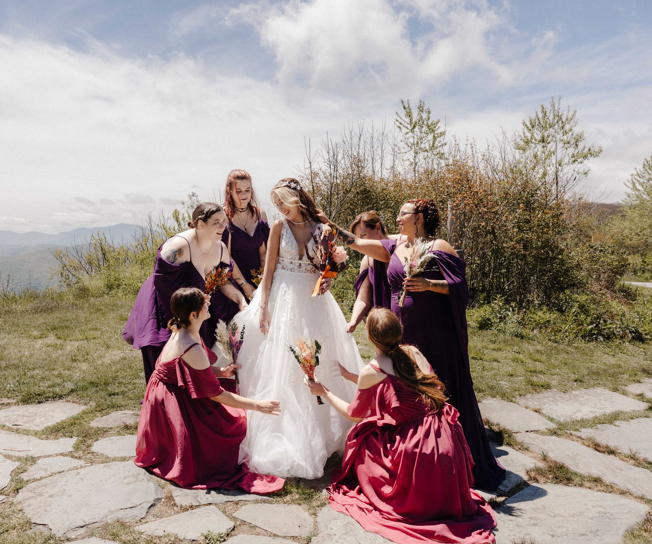Bridesmaids surrounding bride adjusting her dress on mountain