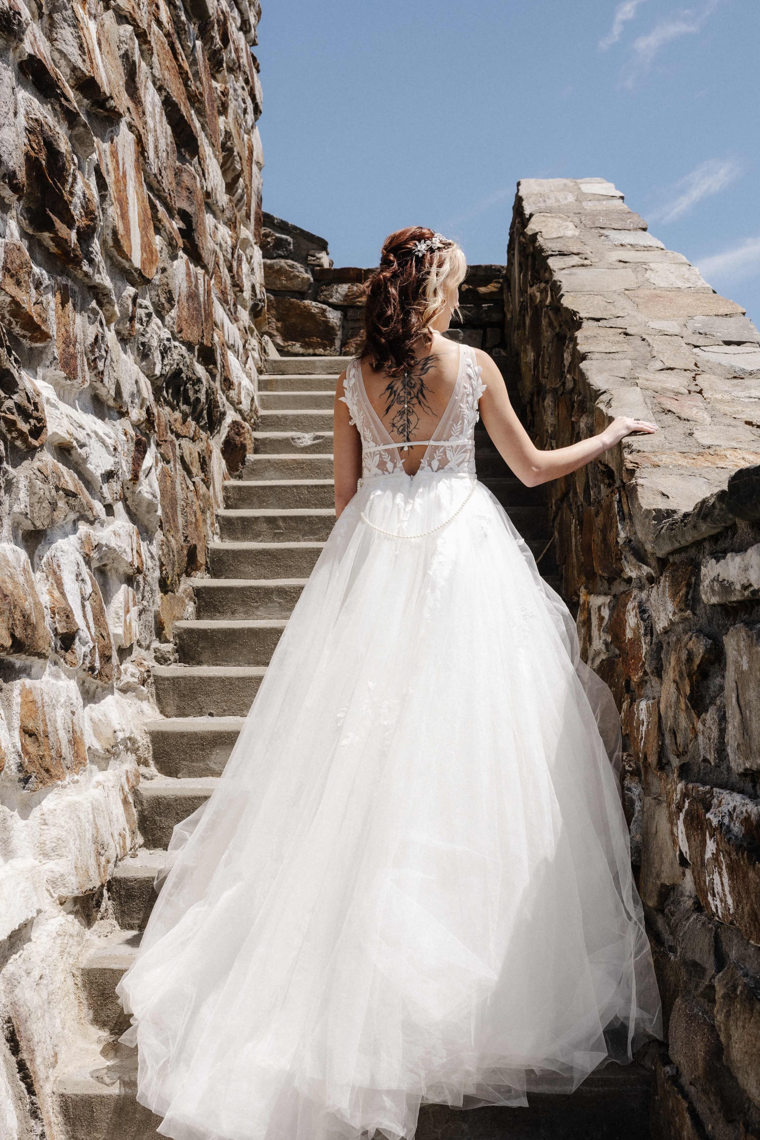 Bride from behind walking up stone stairs showing back tattoo