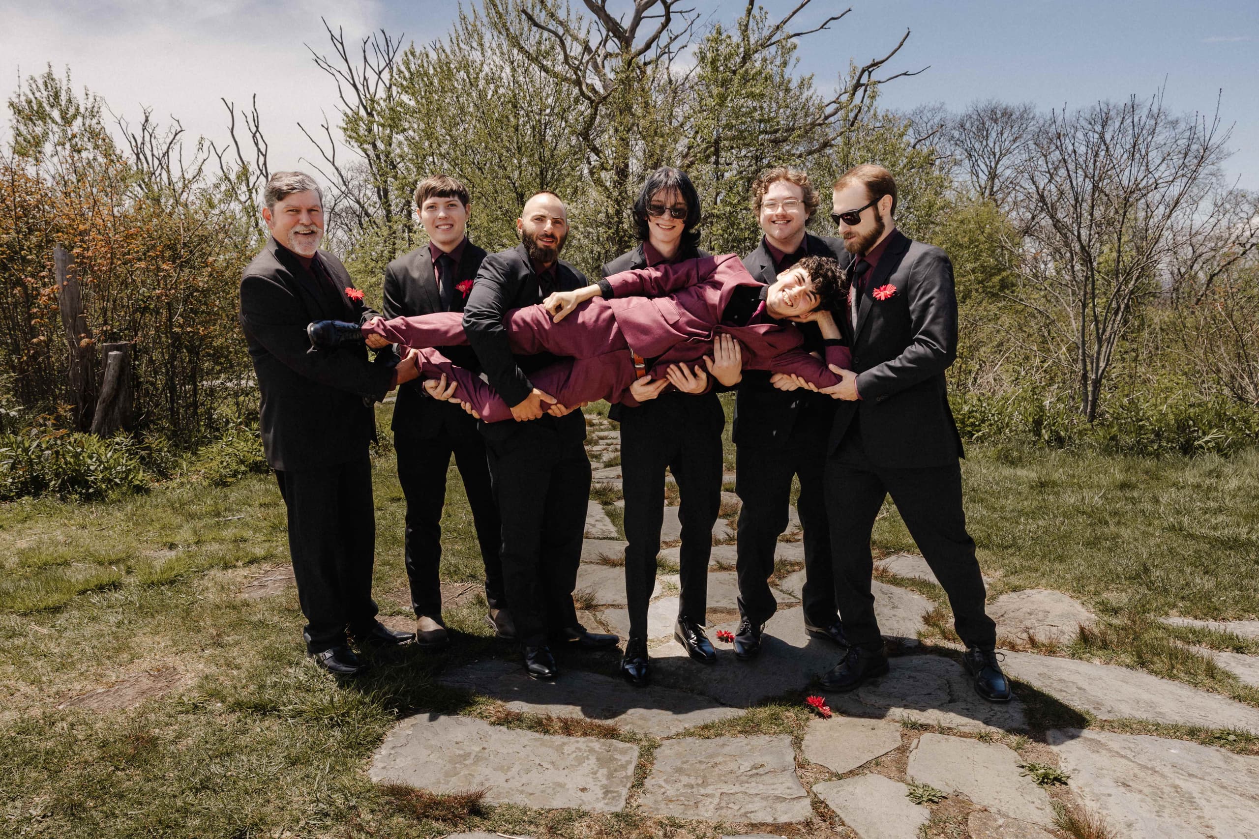 Groomsmen in black suits carrying groom horizontally for fun photo