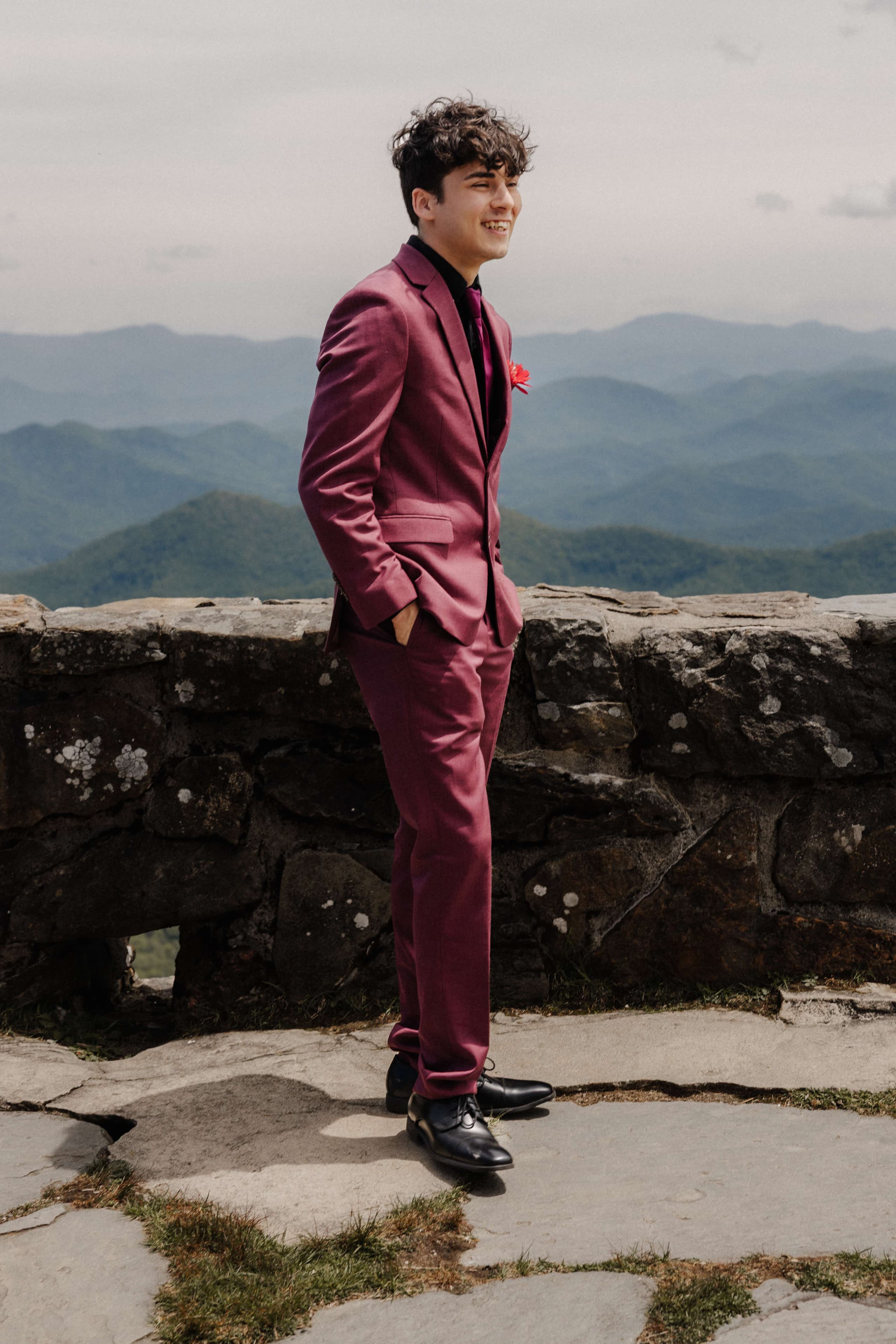 Groom laughing in burgundy suit with mountain backdrop