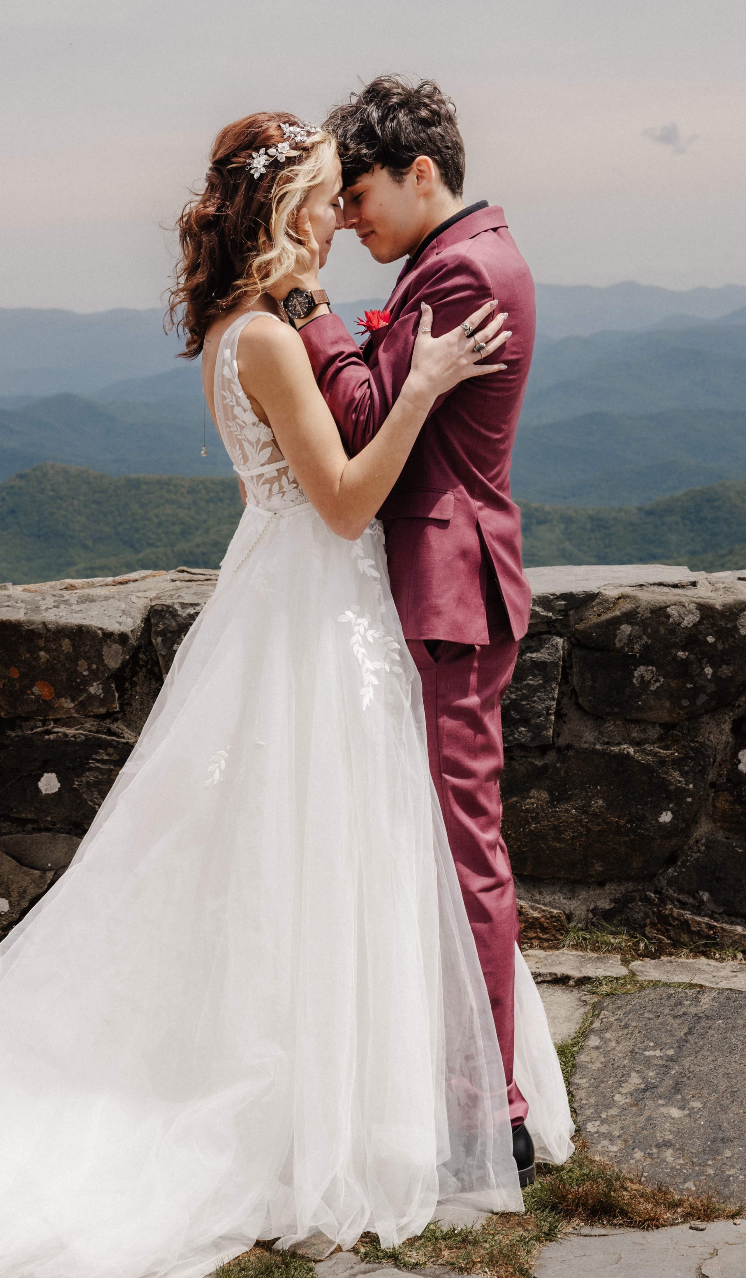 Romantic couple portrait with bride in white dress and groom in burgundy suit at mountain overlook