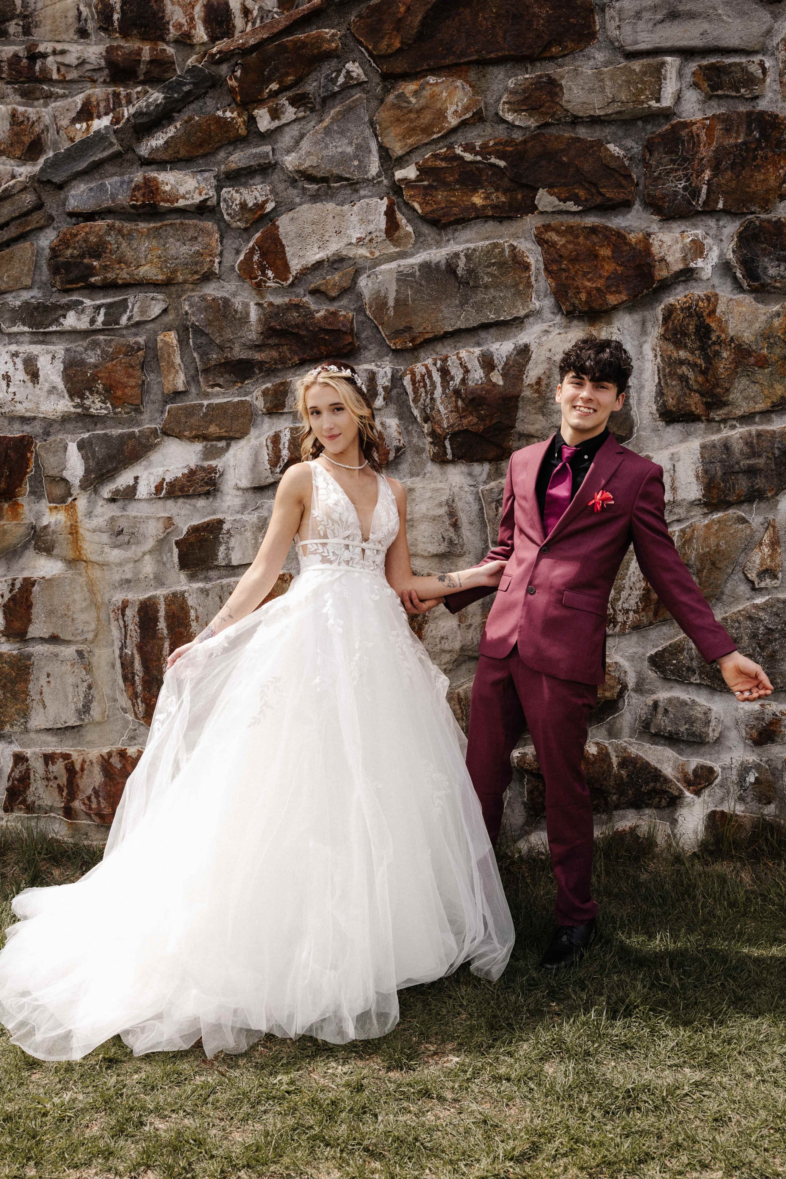 Couple holding hands against stone wall with ballgown flowing