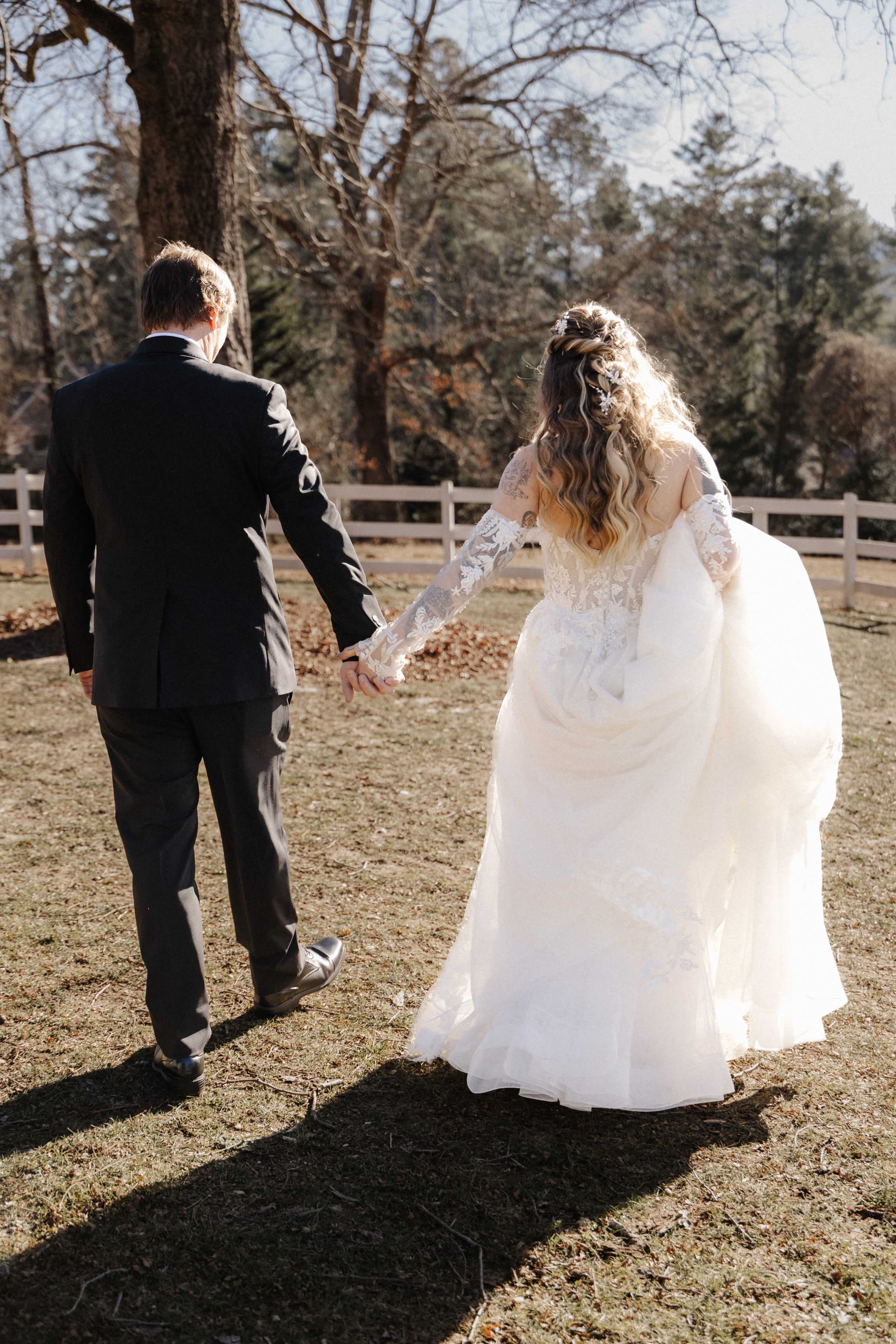 Couple walking away holding hands on farm with white fence