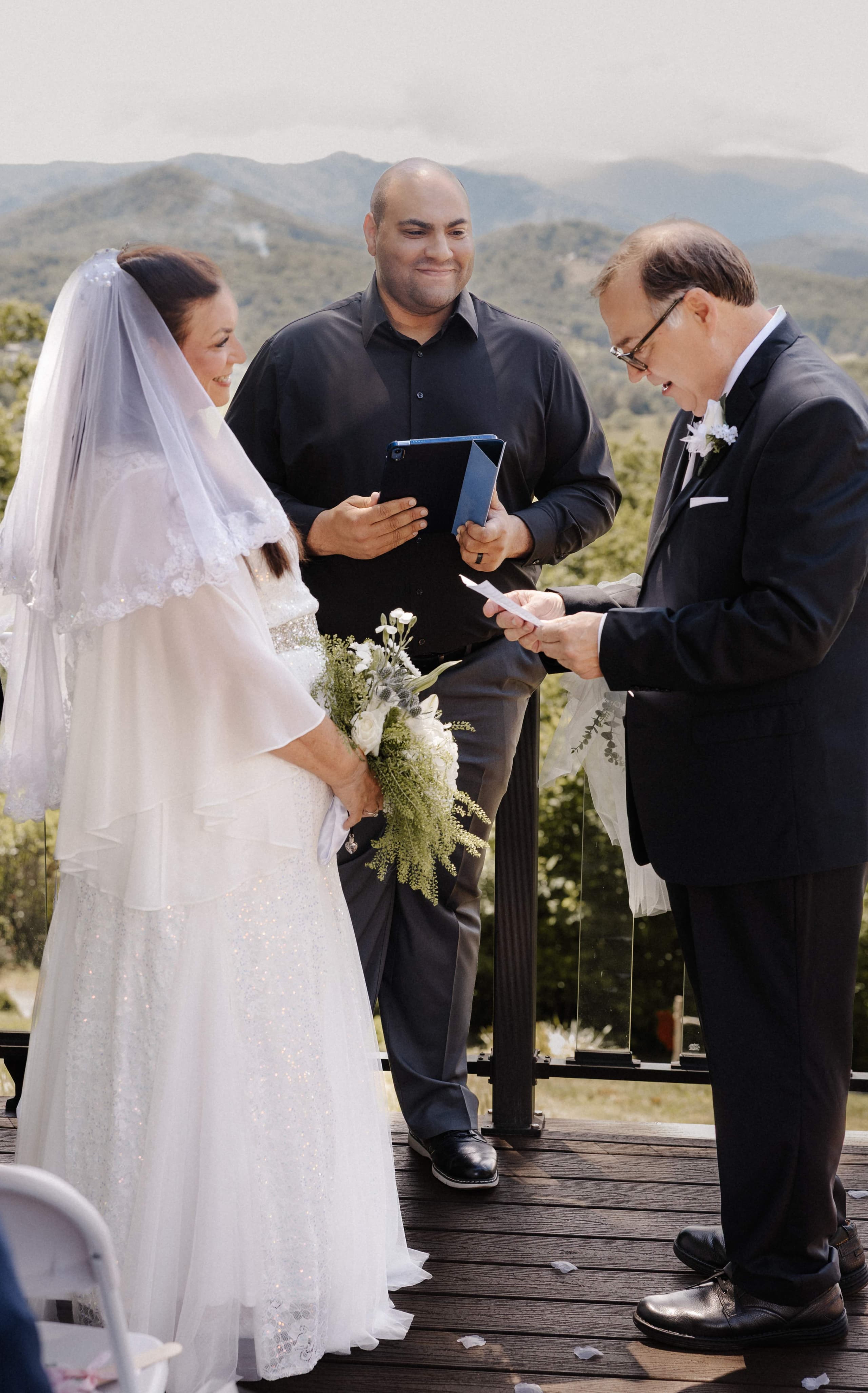 Groom reading vows during ceremony on deck with mountain backdrop