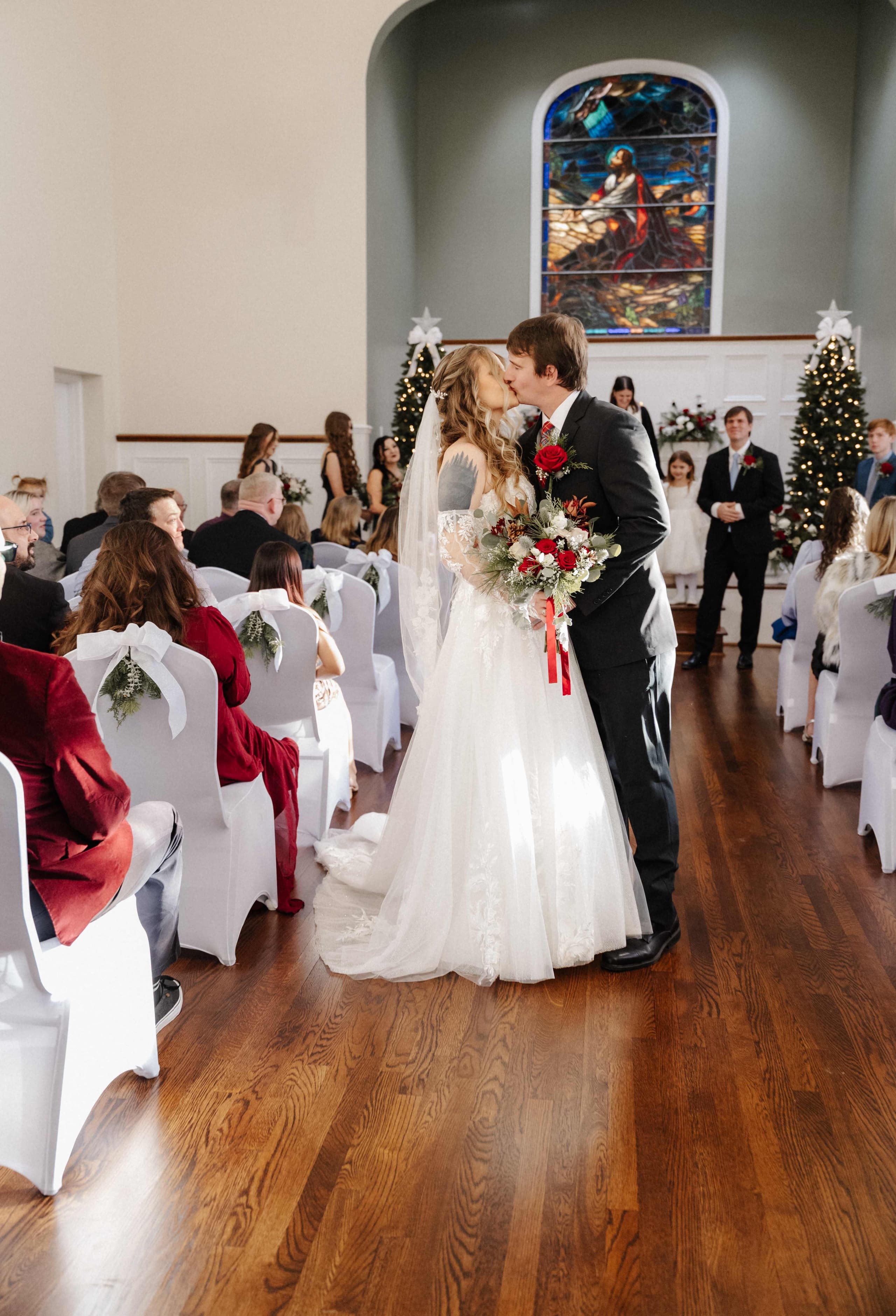 Ceremony kiss in chapel with stained glass window and Christmas trees